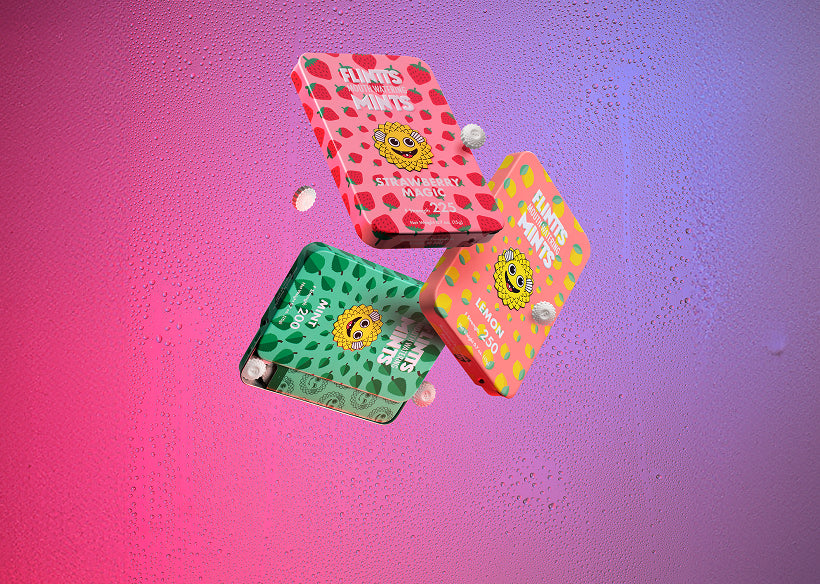 Three colorful Flintts Mints tins—Strawberry Magic, Lemon, and Sour Watermelon—floating against a vibrant, dewy pink-purple background with tablets in motion.